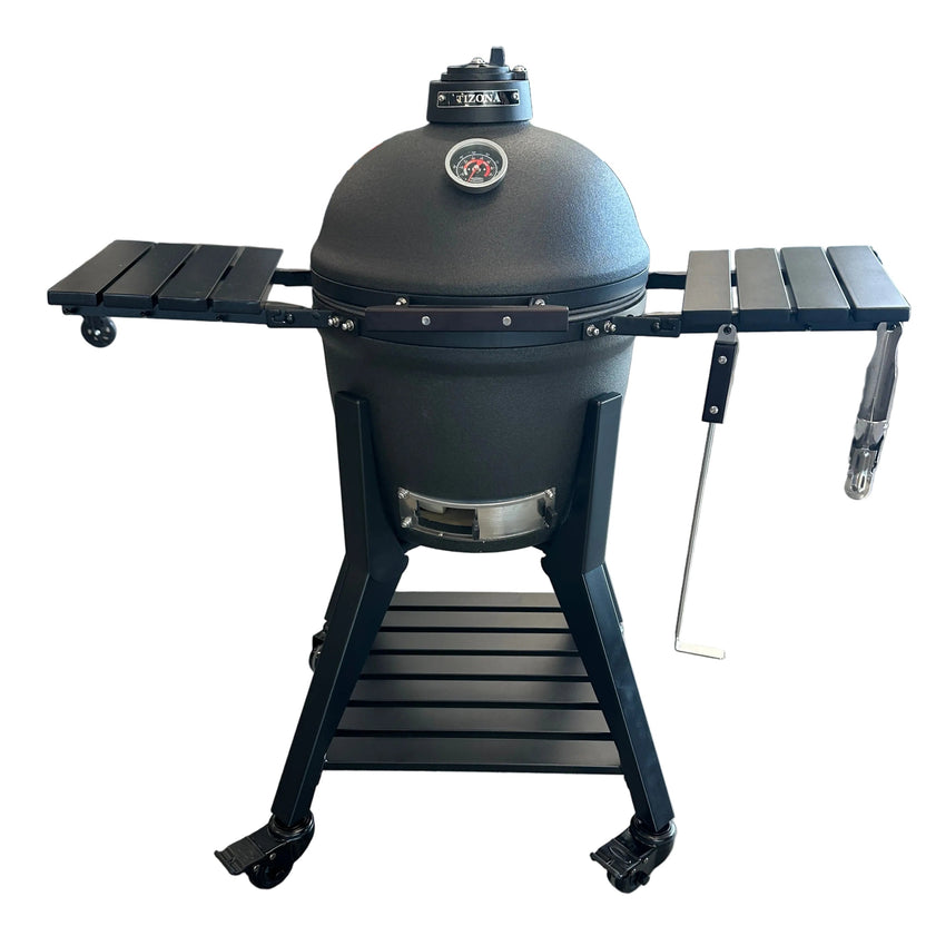 A black Kamadaka ceramic grill with side tables and a lower shelf, photographed in a retail store setting on a tiled floor.
