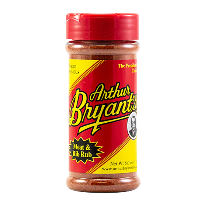 Bottle of Arthur Bryant’s Rib Rub with ribs and BBQ tools on a wooden table