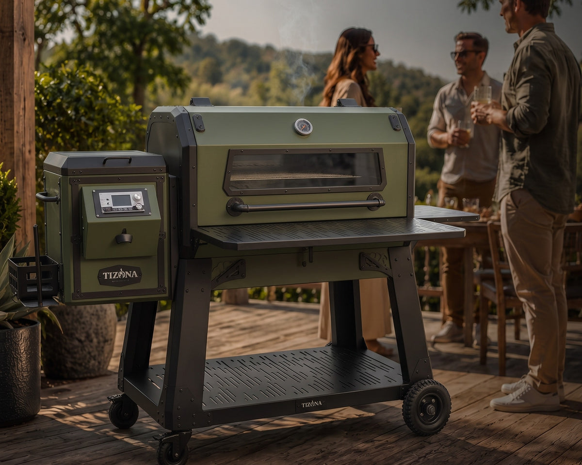 A Tizona kamado grill glowing at dusk on a wooden patio while friends gather around a table strung with lights
